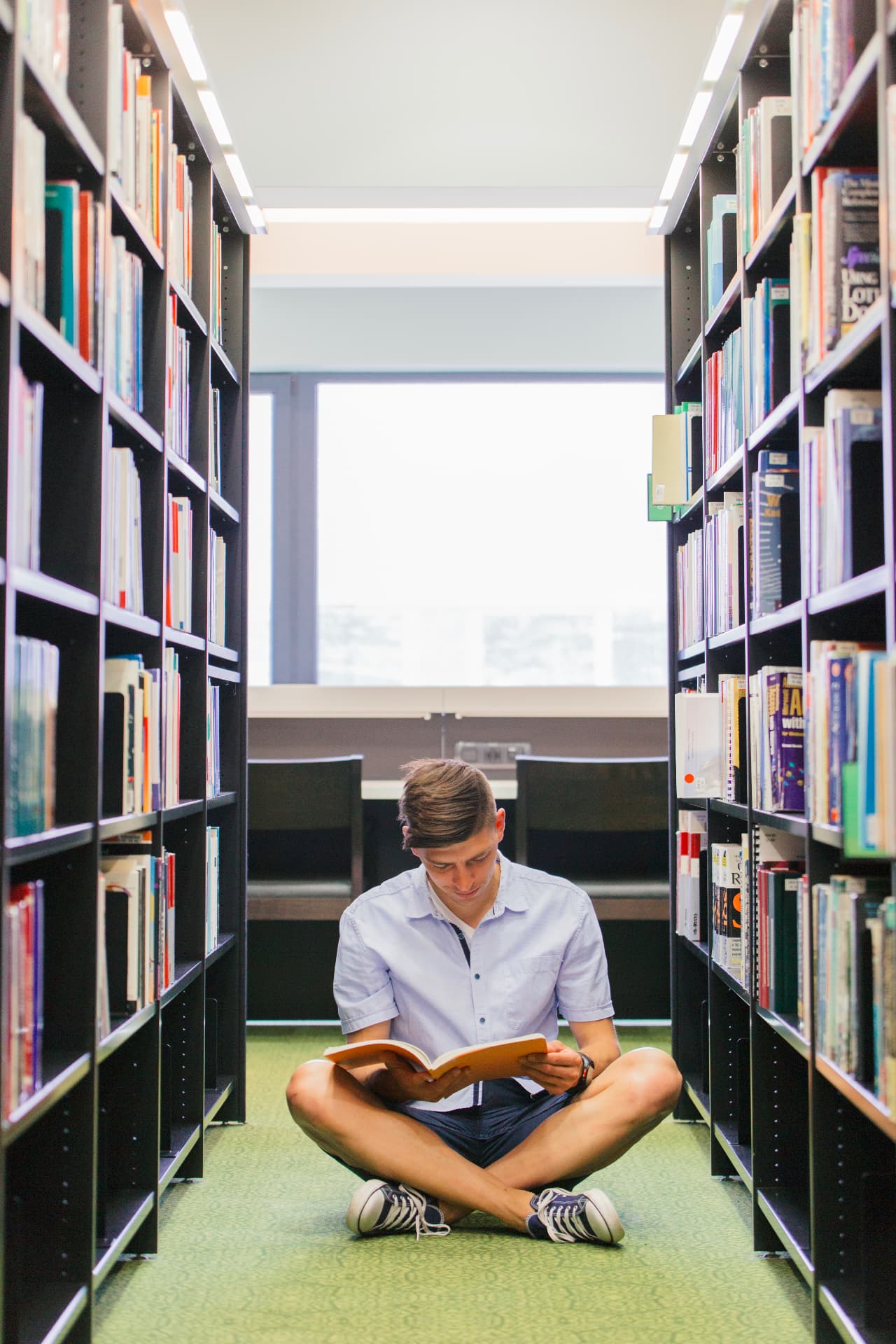 Estudante lendo um livro entre estantes de uma biblioteca.