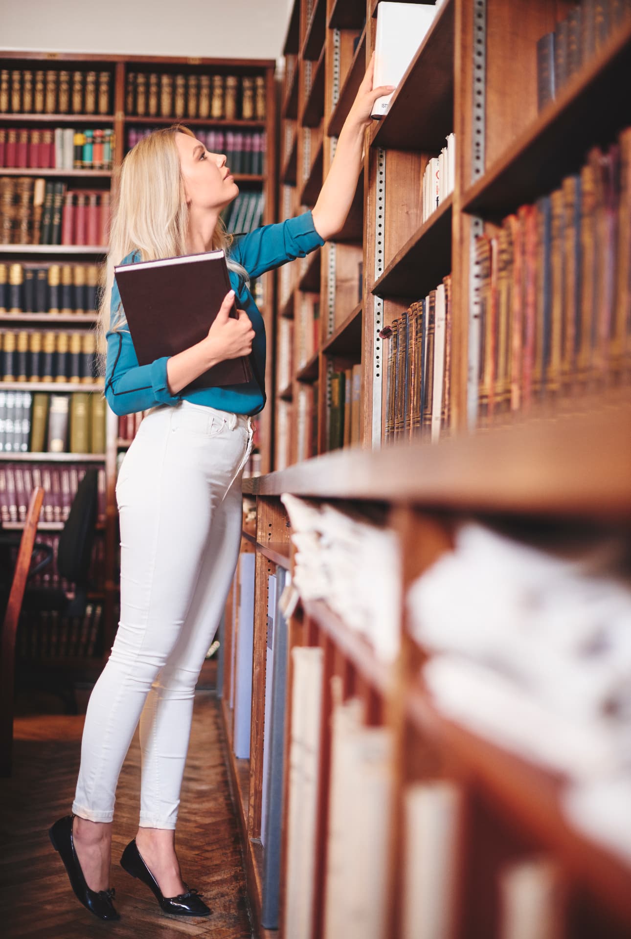 Pesquisadora consultando livros em uma biblioteca acadêmica.