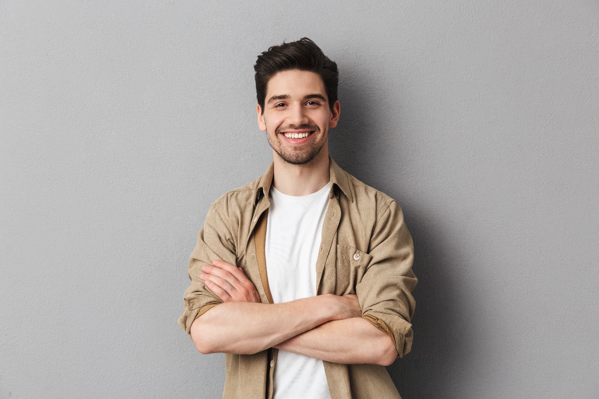 Homem jovem sorrindo com confiança, de braços cruzados.