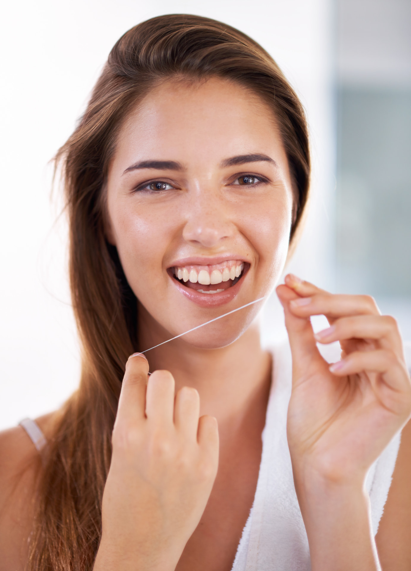 Paciente sorrindo enquanto usa fio dental, representando a facilidade de higiene com dentes alinhados.